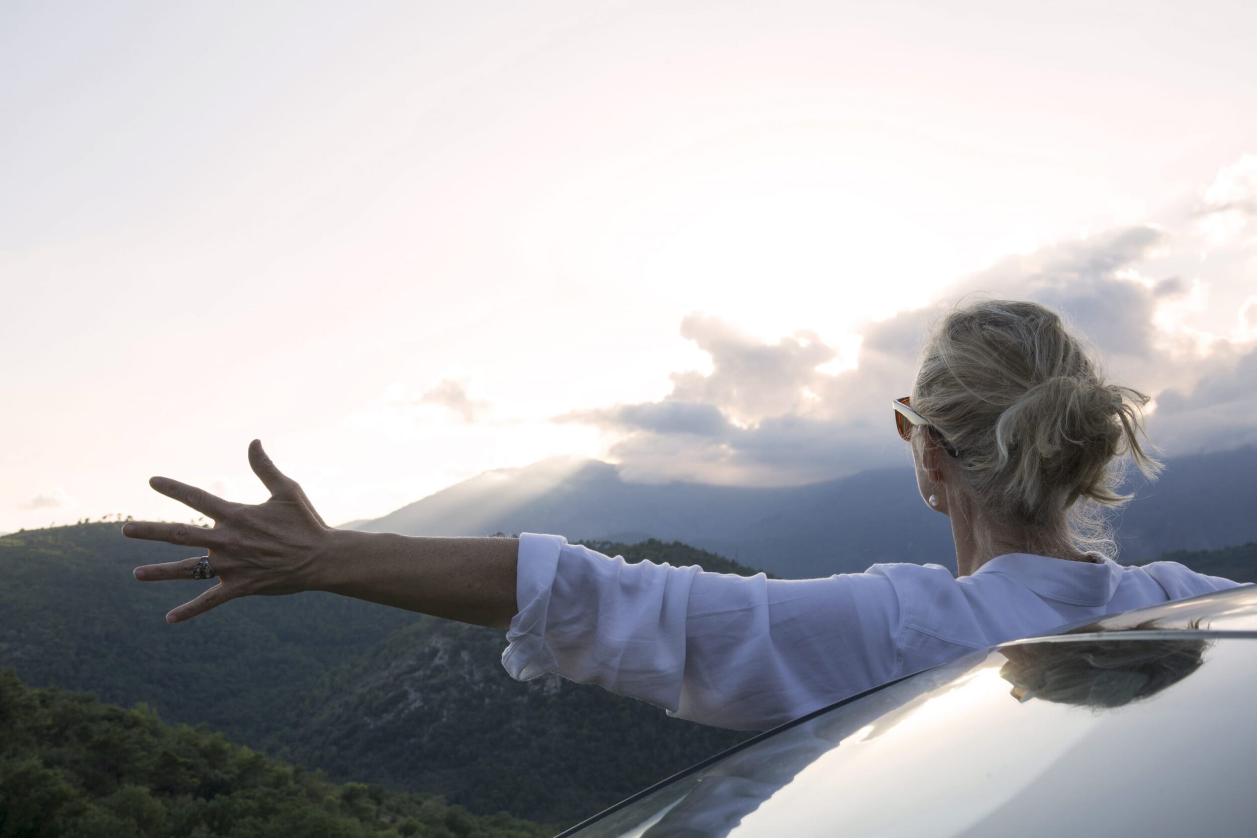 Una donna è in piedi accanto alla propria auto con il viso rivolto verso il paesaggio.