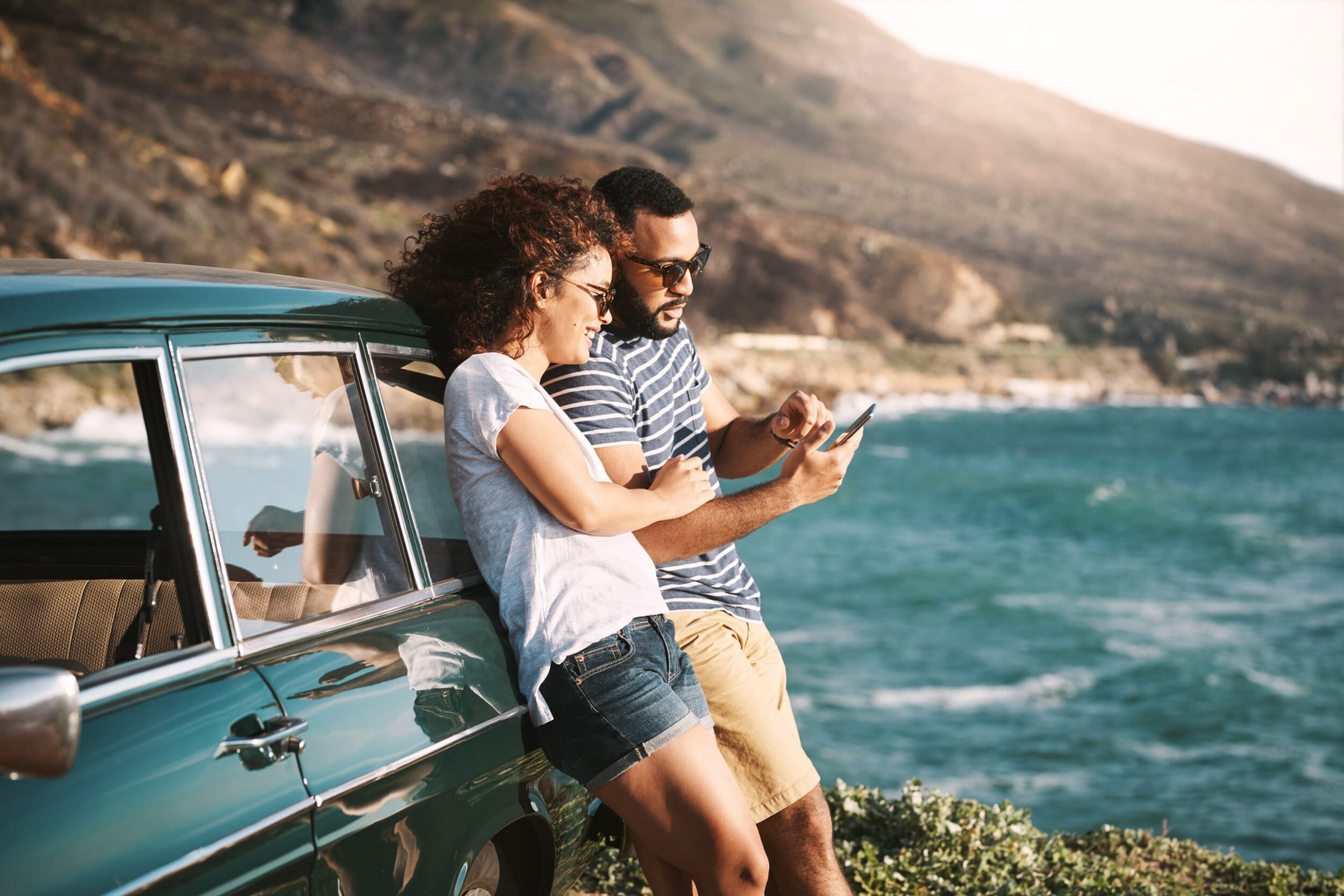 Una donna e un uomo sono appoggiati a un’auto verde. Entrambi indossano gli occhiali da sole.