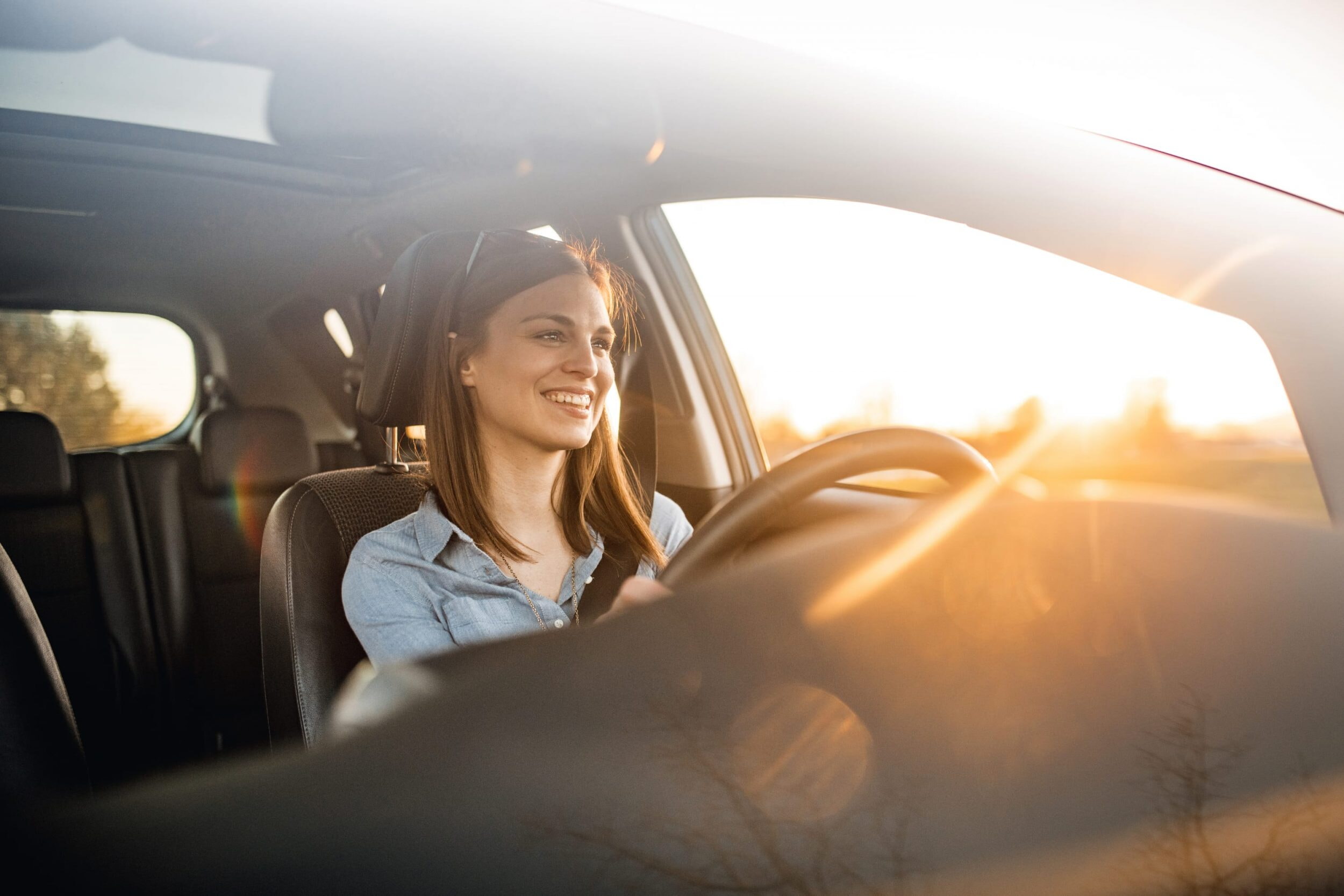 Eine Frau fährt in einem Auto. Die Sonne geht auf. Die dunkelhaarige Frau trägt eine Sonnenbrille.