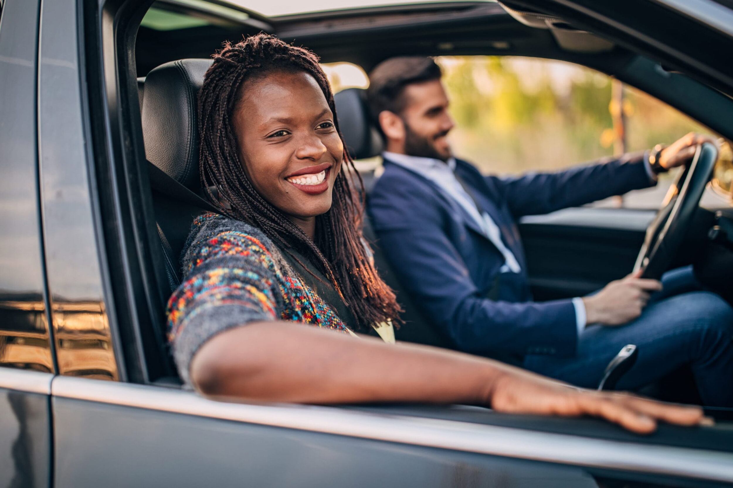 Un uomo in abito blu guida un’auto. La donna accanto guarda fuori dal finestrino.
