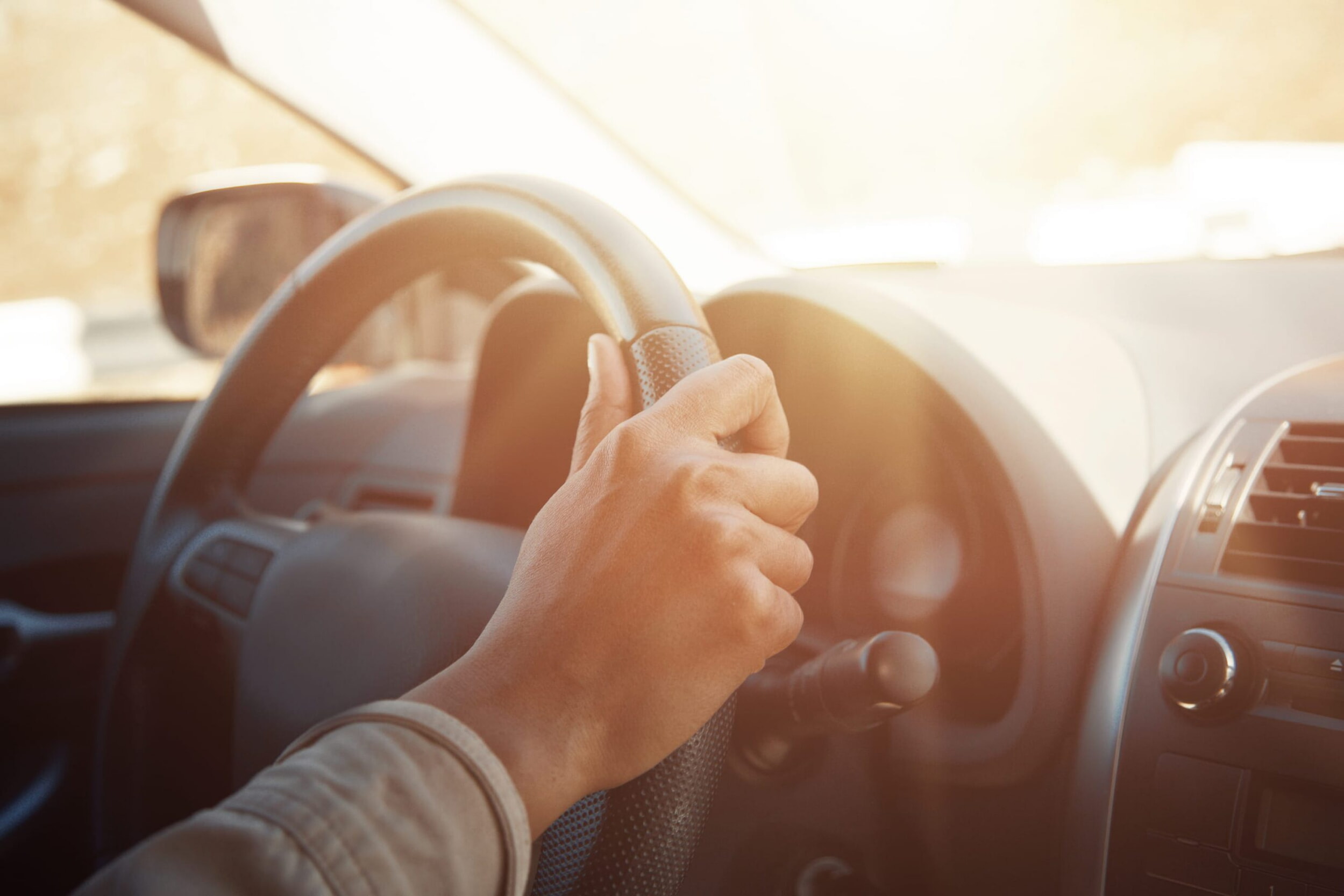 On voit le volant d’une voiture. Le soleil brille à travers le pare-brise.