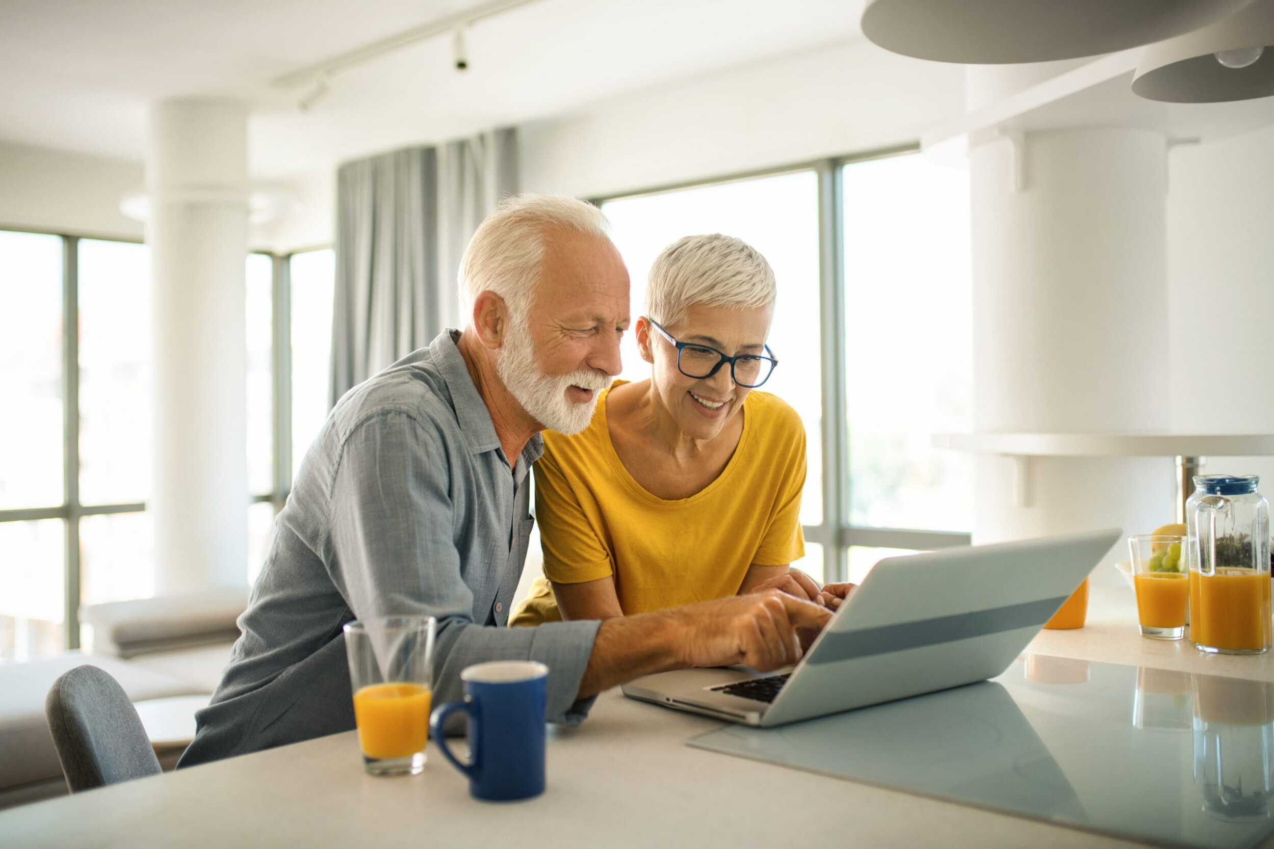 Un uomo più avanti con gli anni e una donna più giovane sono seduti a un tavolo davanti a un laptop.