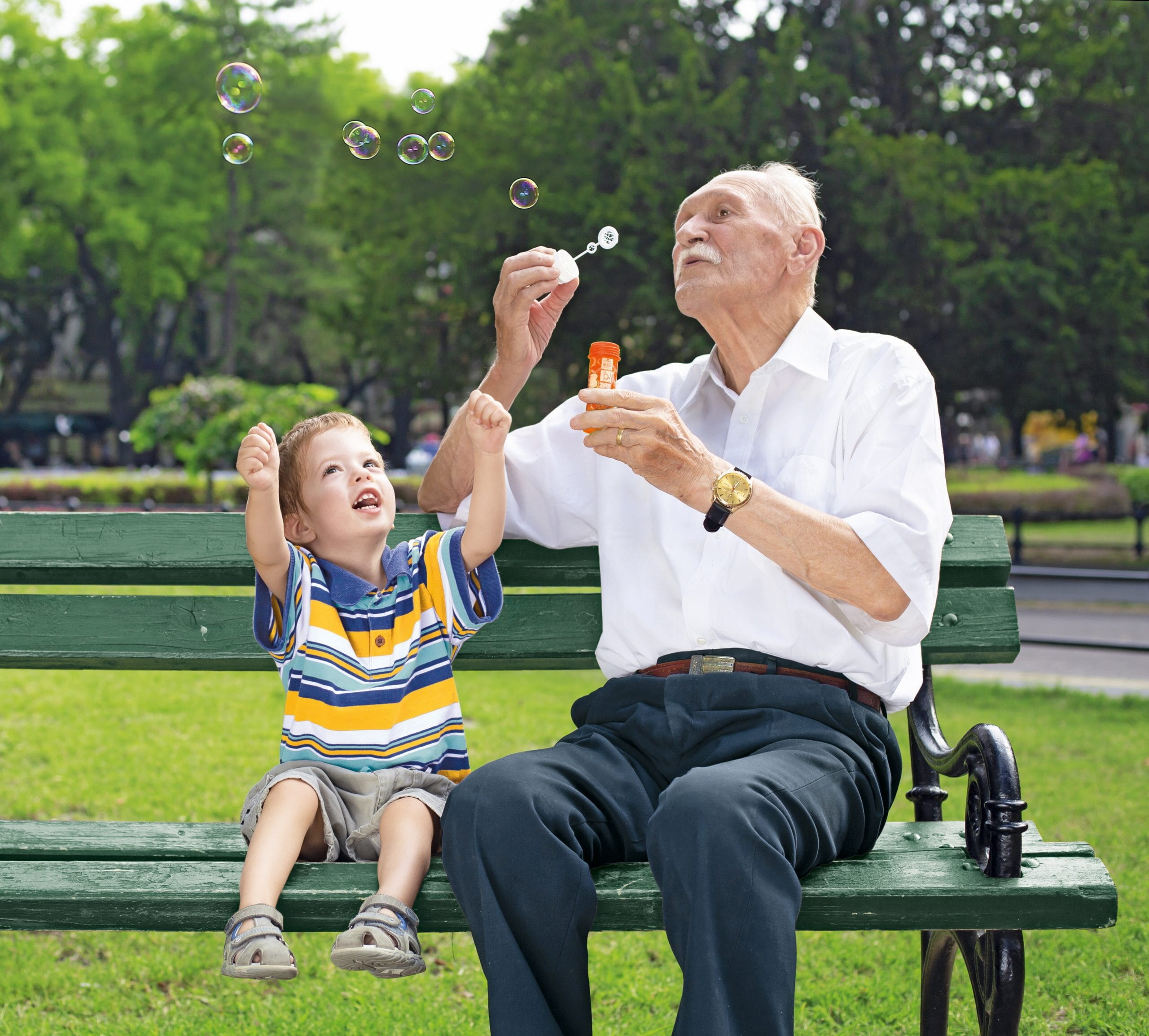 grandfather blowing soap bubbles to his grandchild on a bench