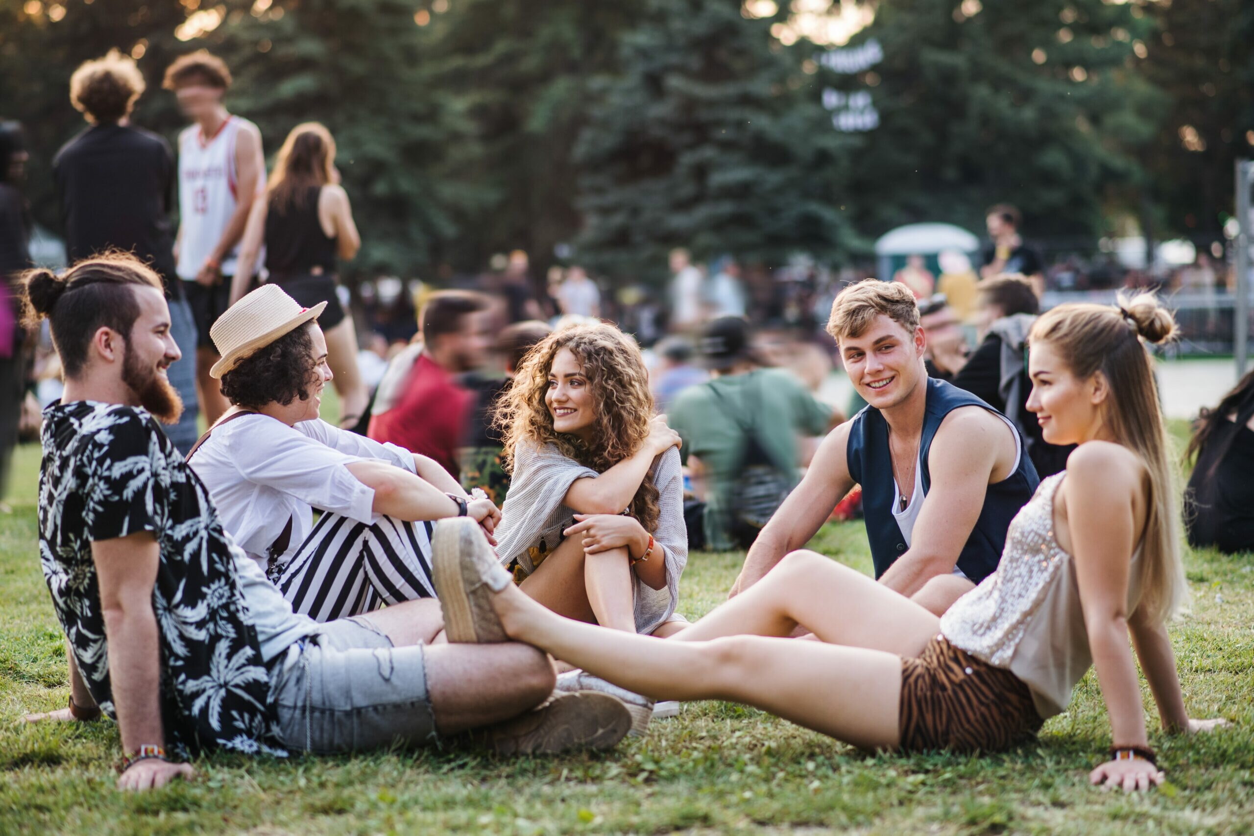 Group Of Young Friends Sitting On Ground At Summer Festival.