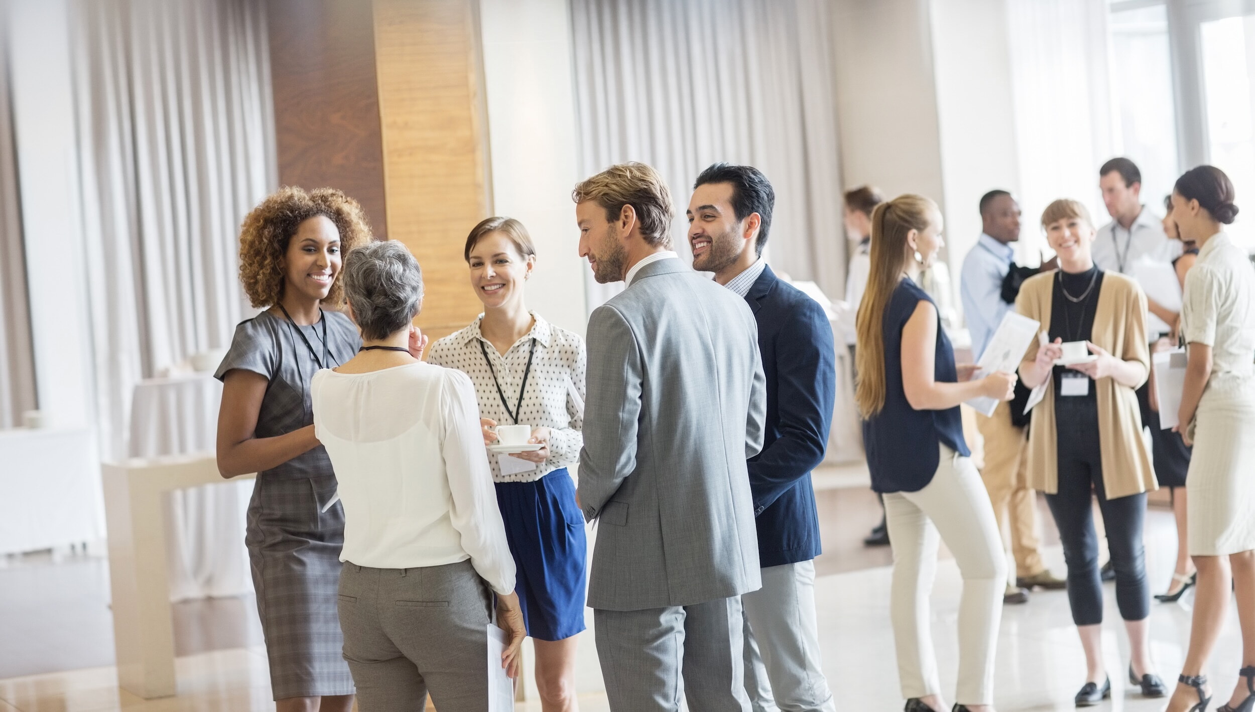 Group Of Business People Standing In Hall, Smiling And Talking Together