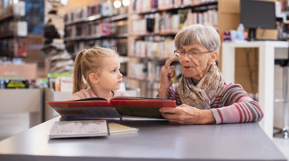 Grandmother Reads A Book To Her Granddaughter In The Library