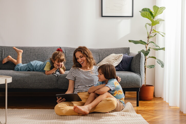 Happy Family Moments: The Mother Sits On The Floor And Watches Something On The Digital Tablet With Her Kids